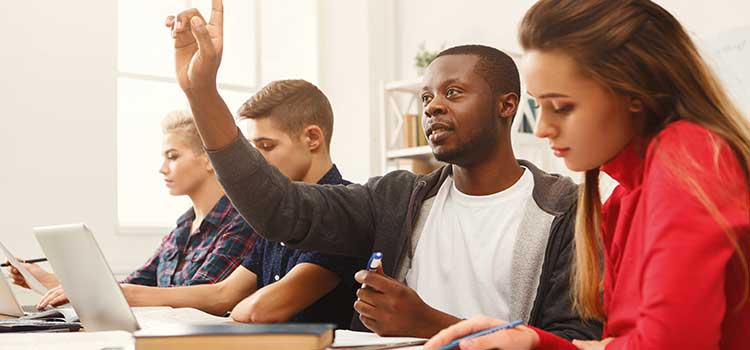 man raises hand in college class