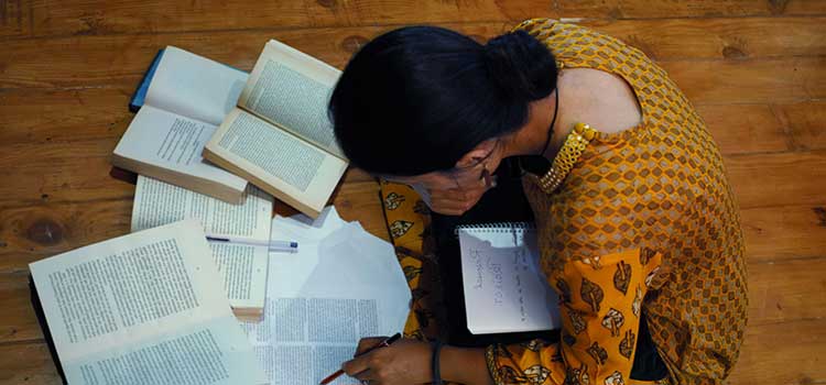 woman sits on floor with books around her and studies