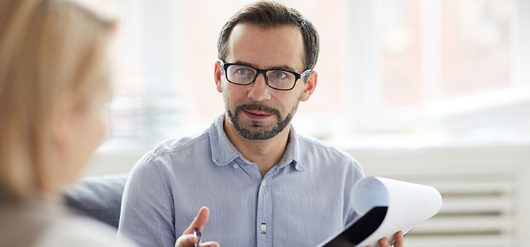 man with notepad and pen talking from patient point of view in foreground