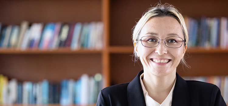 smiling woman sits in front of bookcases full of books