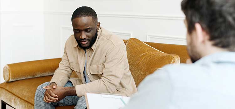 counselor speaks with circumspect patient sitting on sofa