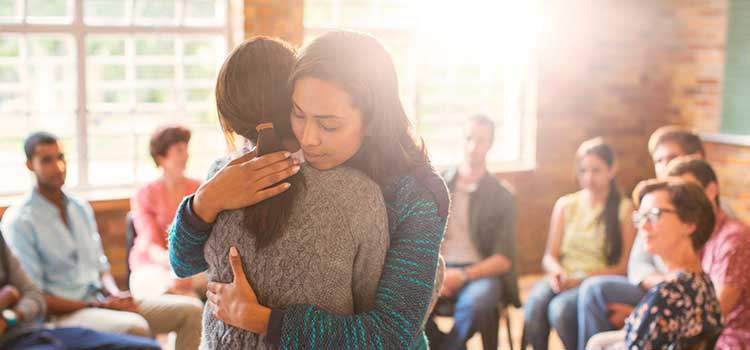 a peer support specialist hugs someone in a support group